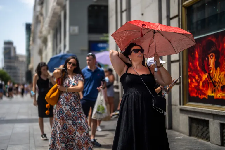 A woman shields herself from the sun with a red umbrella during a heatwave on a city street