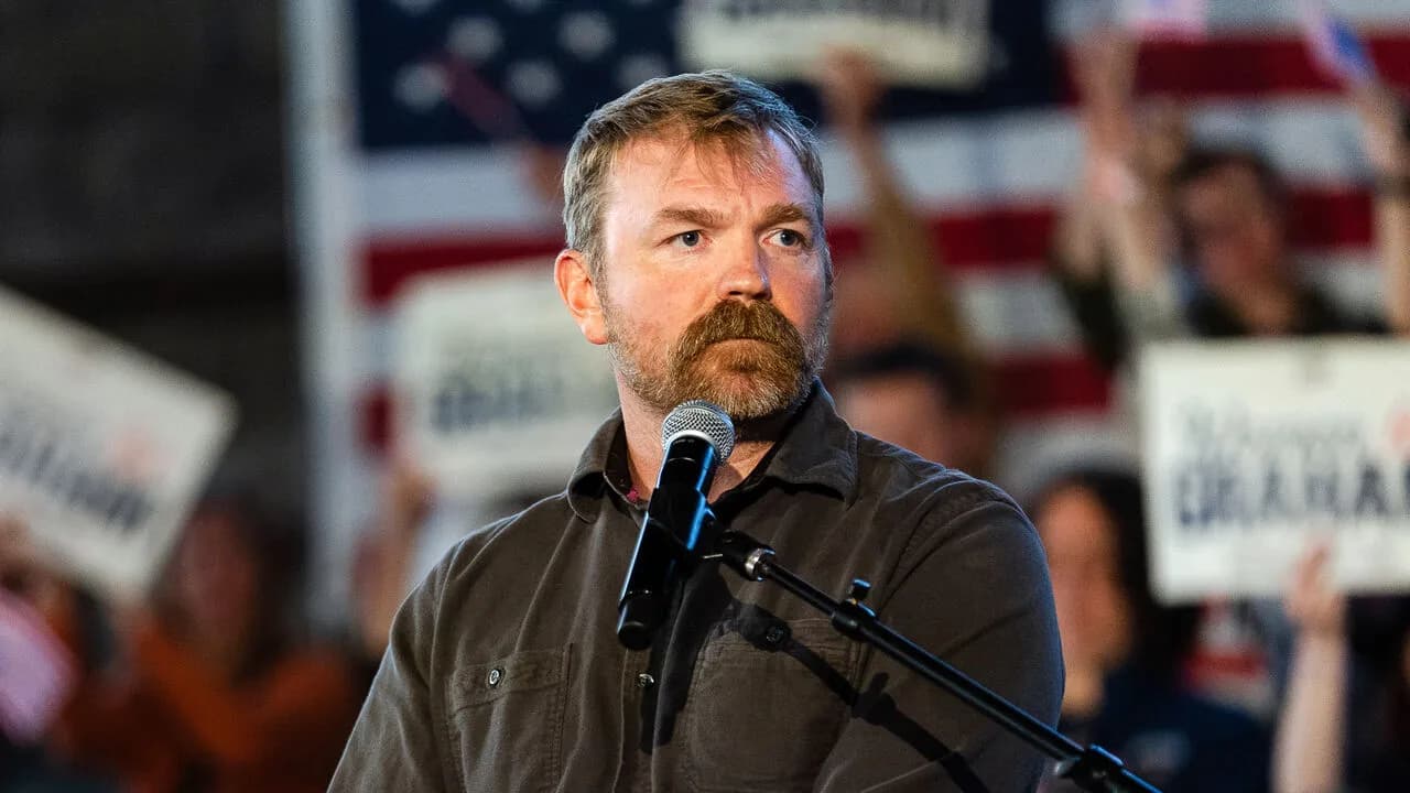Graham Platner, the Maine Senate candidate, stands at a microphone before an American flag at a campaign rally