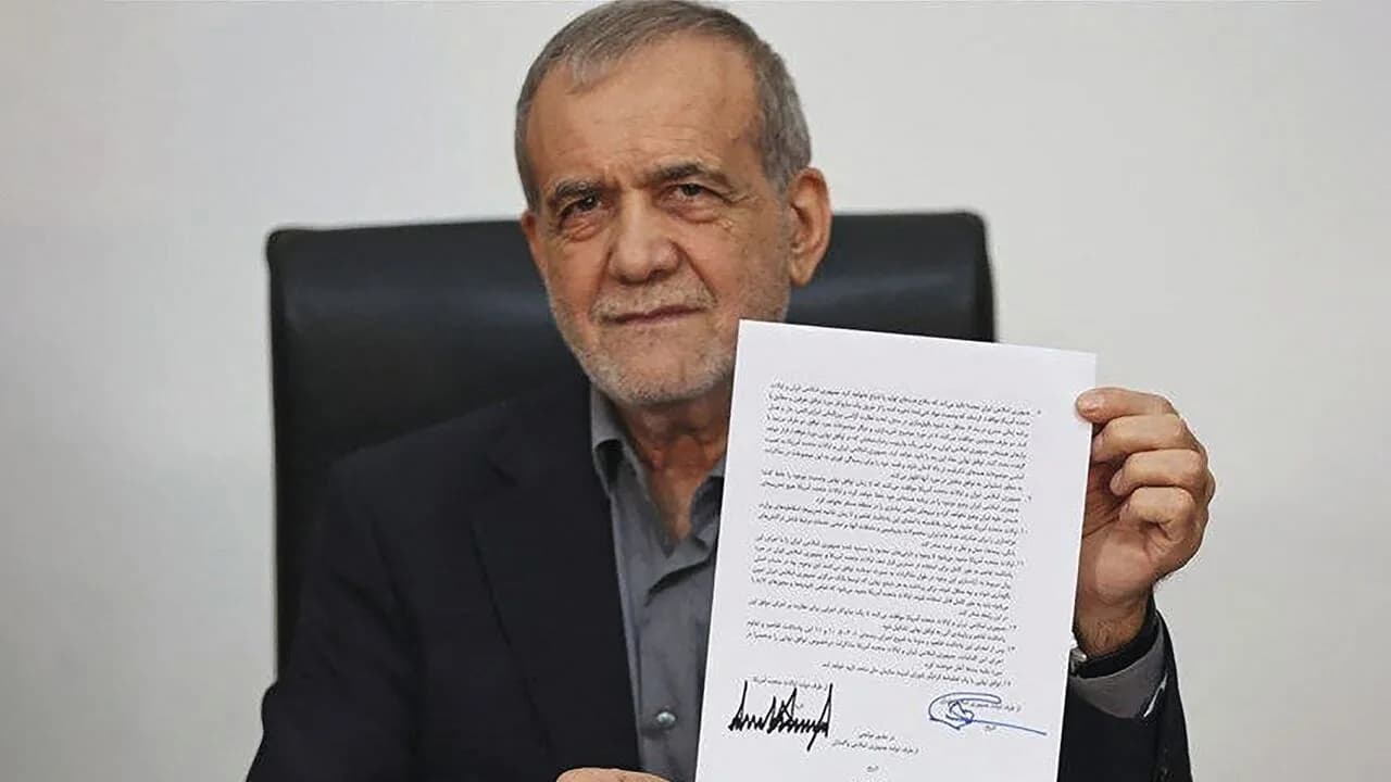 Iran's president sits at a desk holding up a signed document covered in Persian text