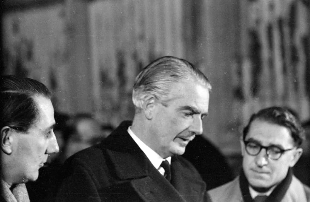 British Prime Minister Anthony Eden in a dark overcoat among aides in a black and white photograph
