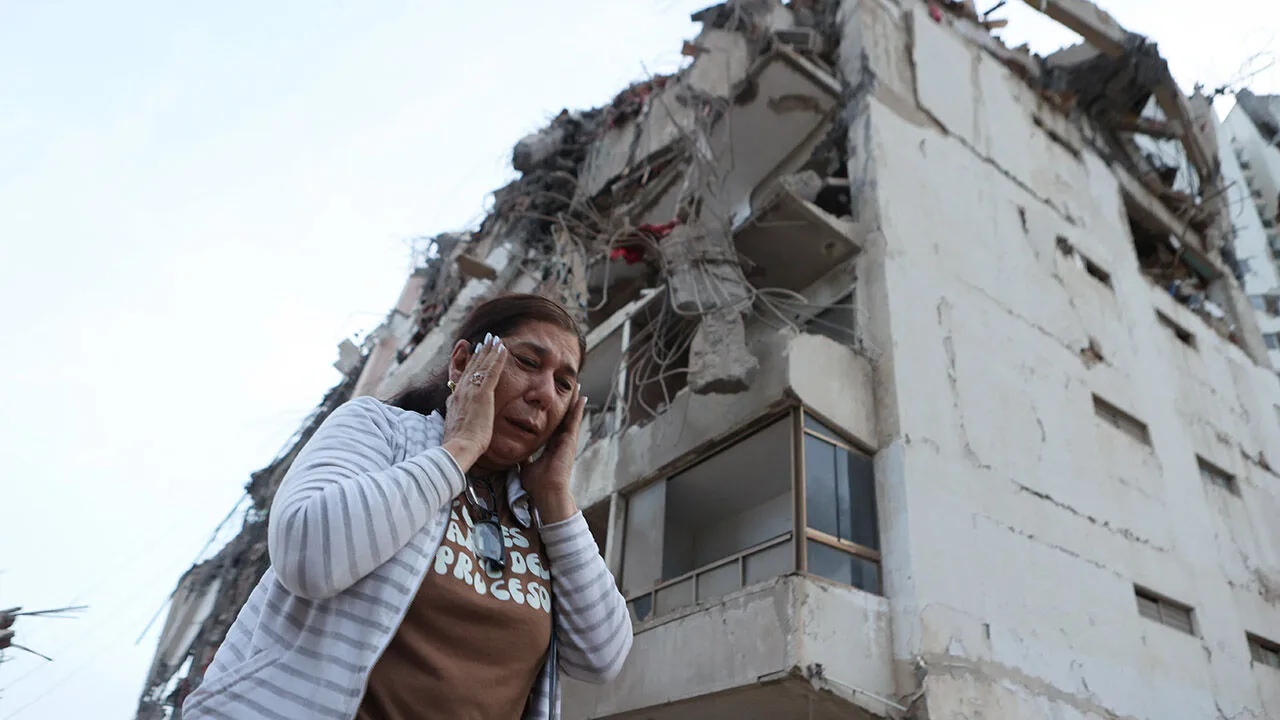 A woman weeps in front of a heavily damaged apartment building with its upper floors torn open
