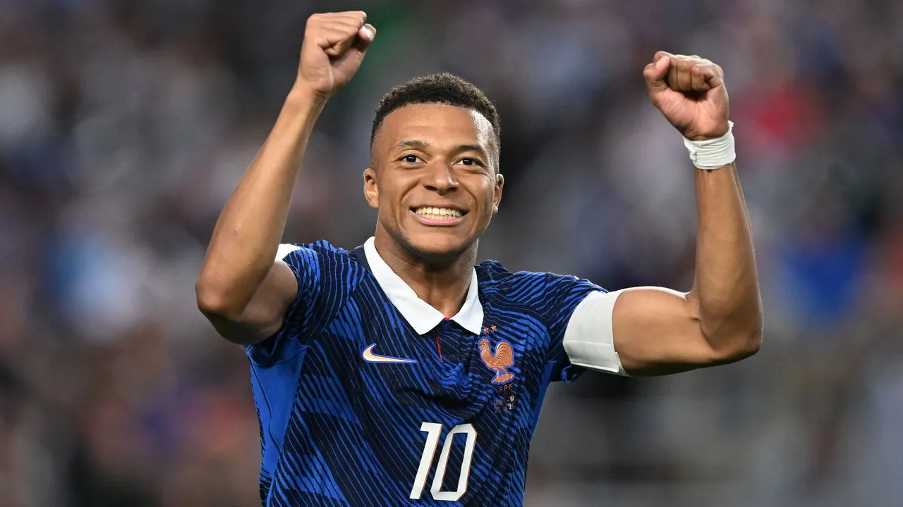 A footballer in a blue France number 10 shirt raises both fists and smiles in celebration on the pitch