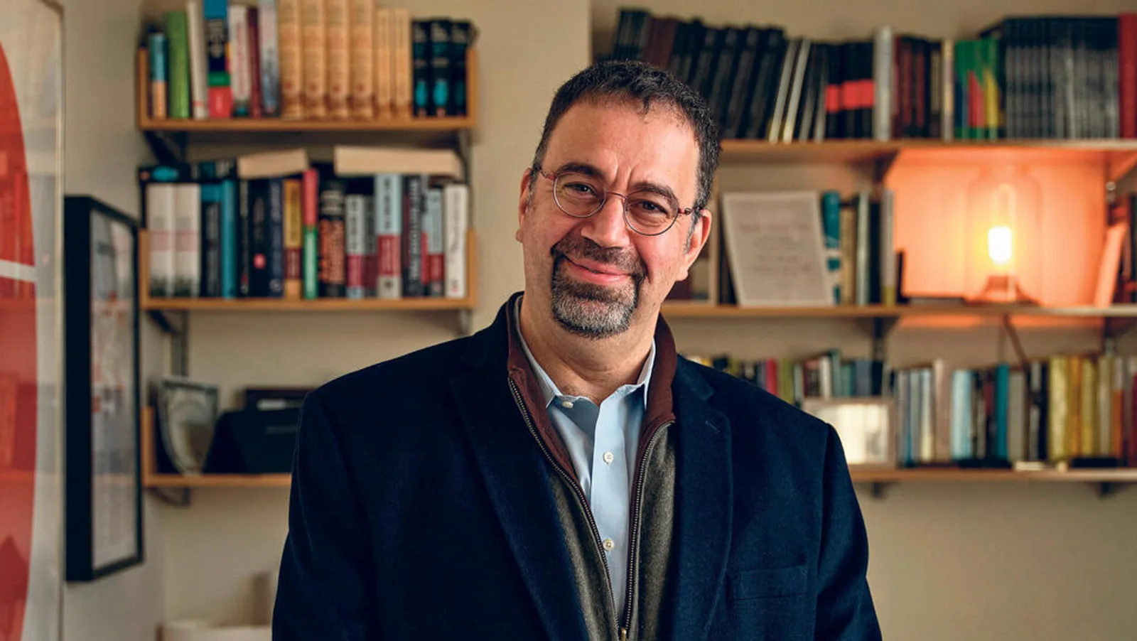 Economist Daron Acemoglu smiling in front of full bookshelves in his study