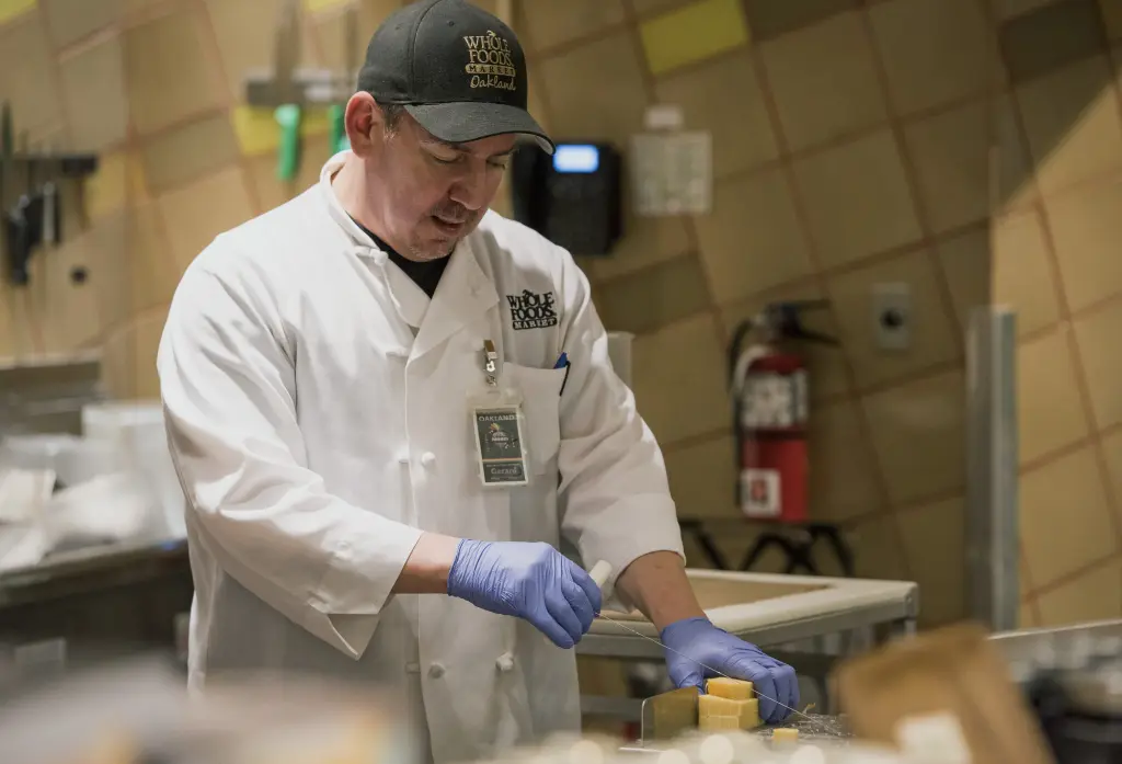 A Whole Foods Market employee prepares cheese in the deli section