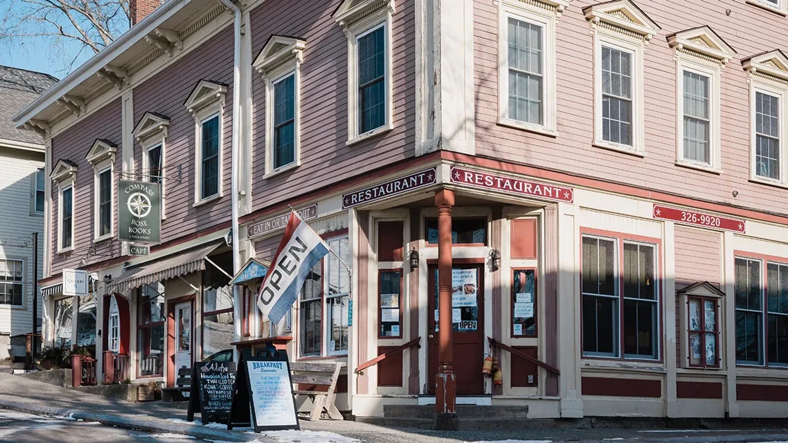 A row of independent shops and a corner restaurant with an open flag on a small-town American main street in winter