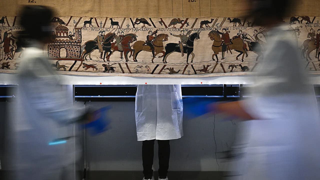 Conservators in white coats work around the Bayeux Tapestry as it is prepared for display