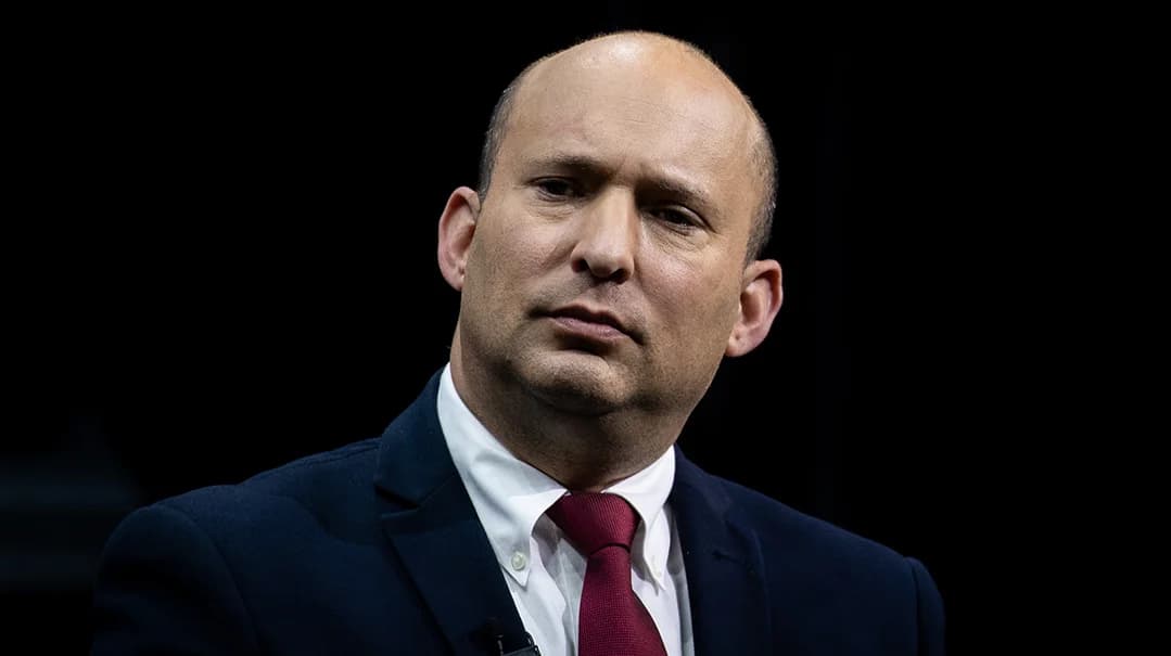 Naftali Bennett in a dark suit and red tie against a black background