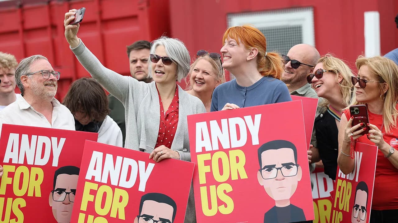 Supporters hold red ANDY FOR US campaign placards, one taking a selfie