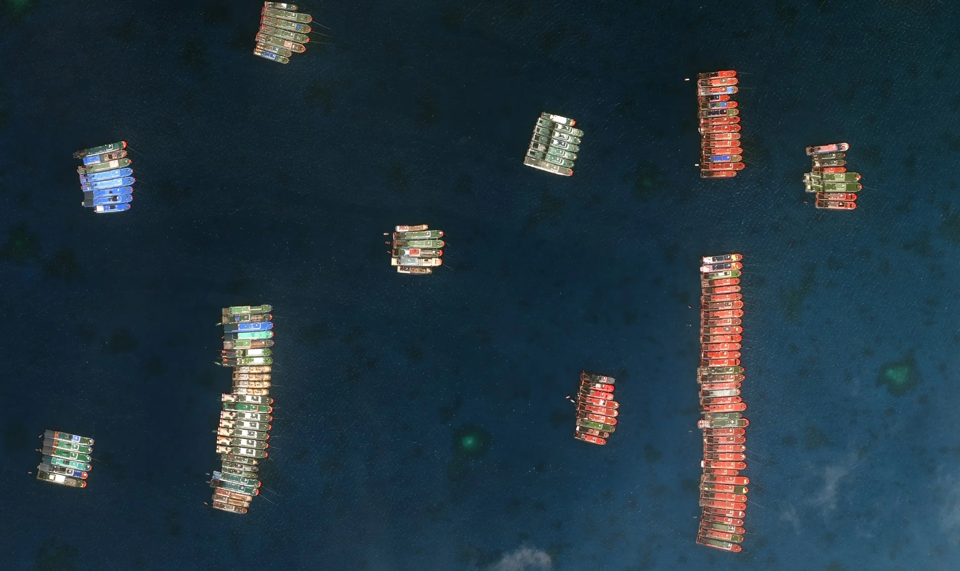 Satellite view of Chinese fishing vessels clustered at anchor over a contested reef in the South China Sea