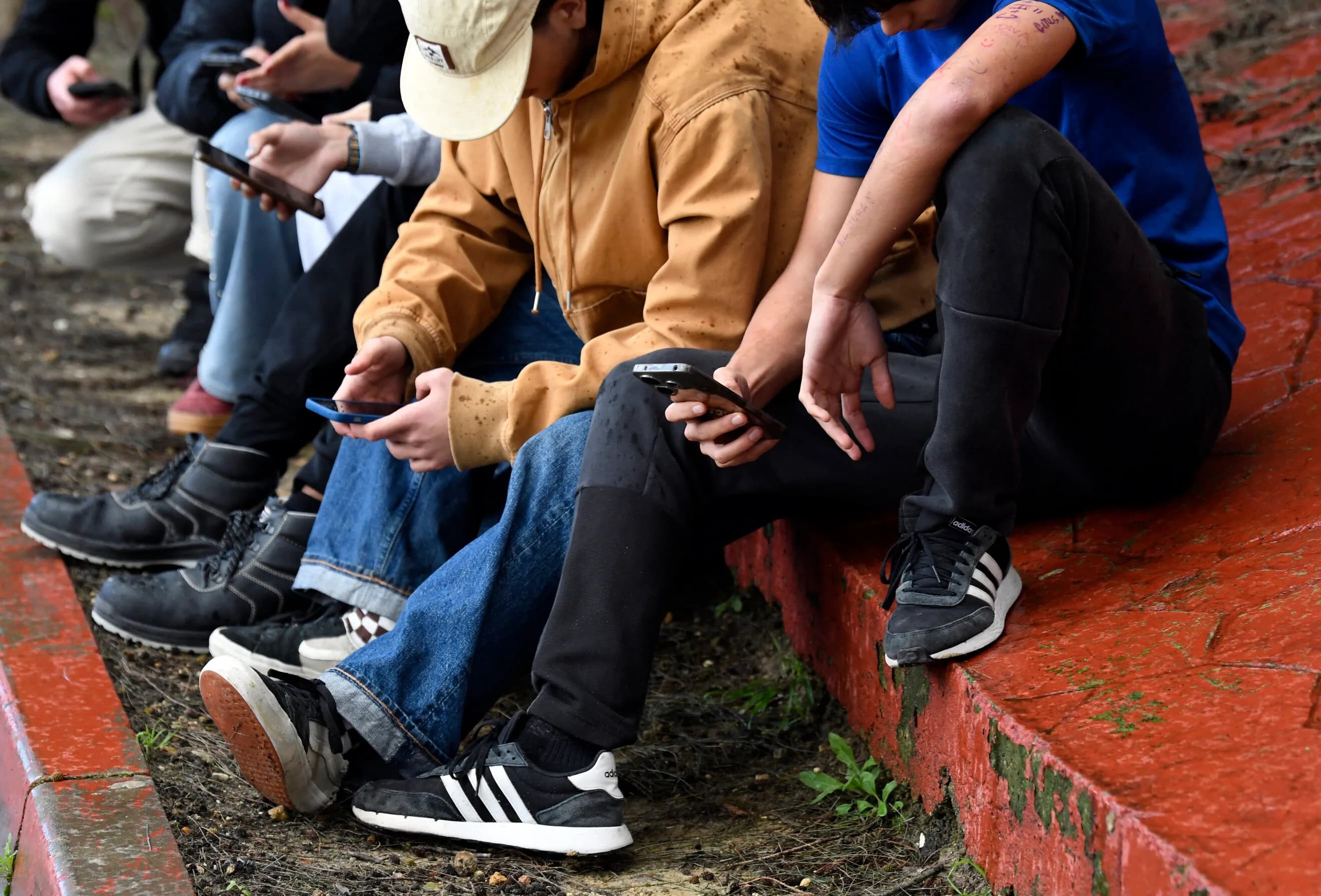 Teenagers sit in a row looking down at their smartphones