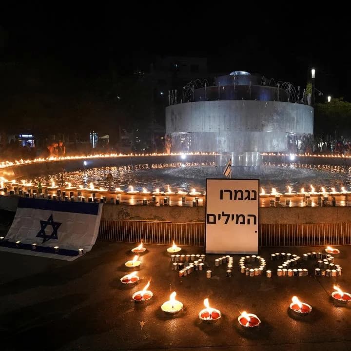 A memorial of candles and an Israeli flag arranged around a fountain in Tel Aviv at night