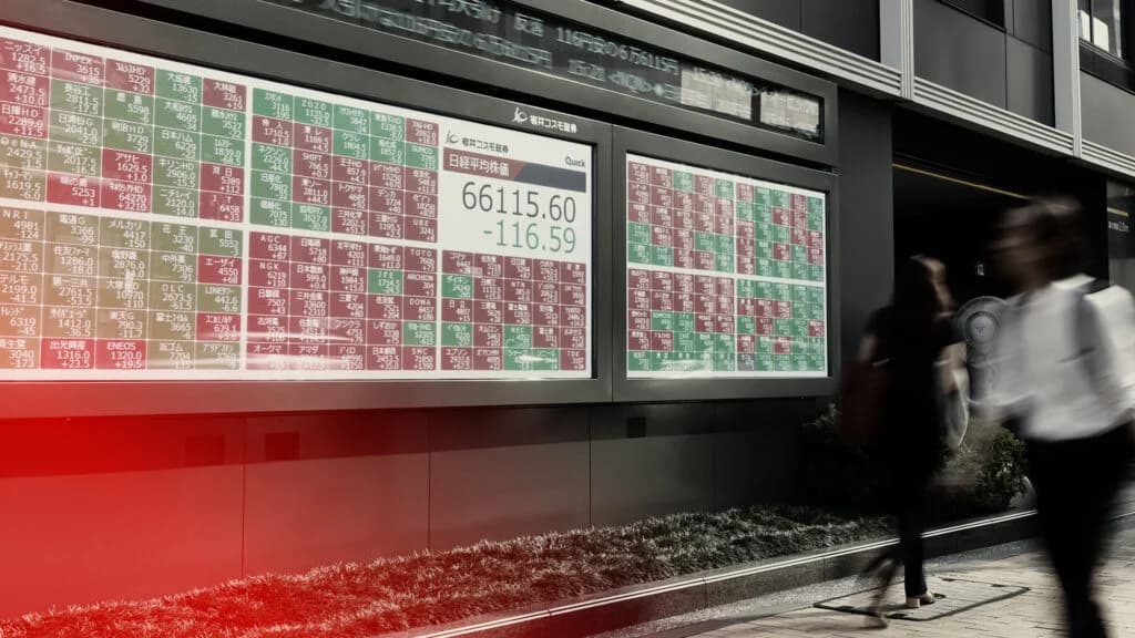A Nikkei stock index board on a Tokyo street shows the index down as pedestrians walk past