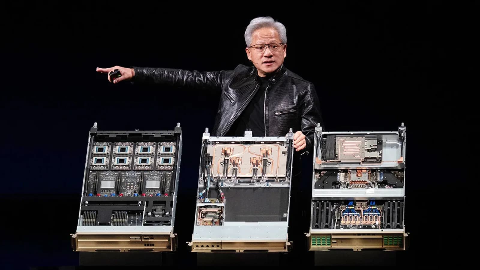Nvidia chief executive Jensen Huang in a black leather jacket gestures on stage beside three opened AI server units