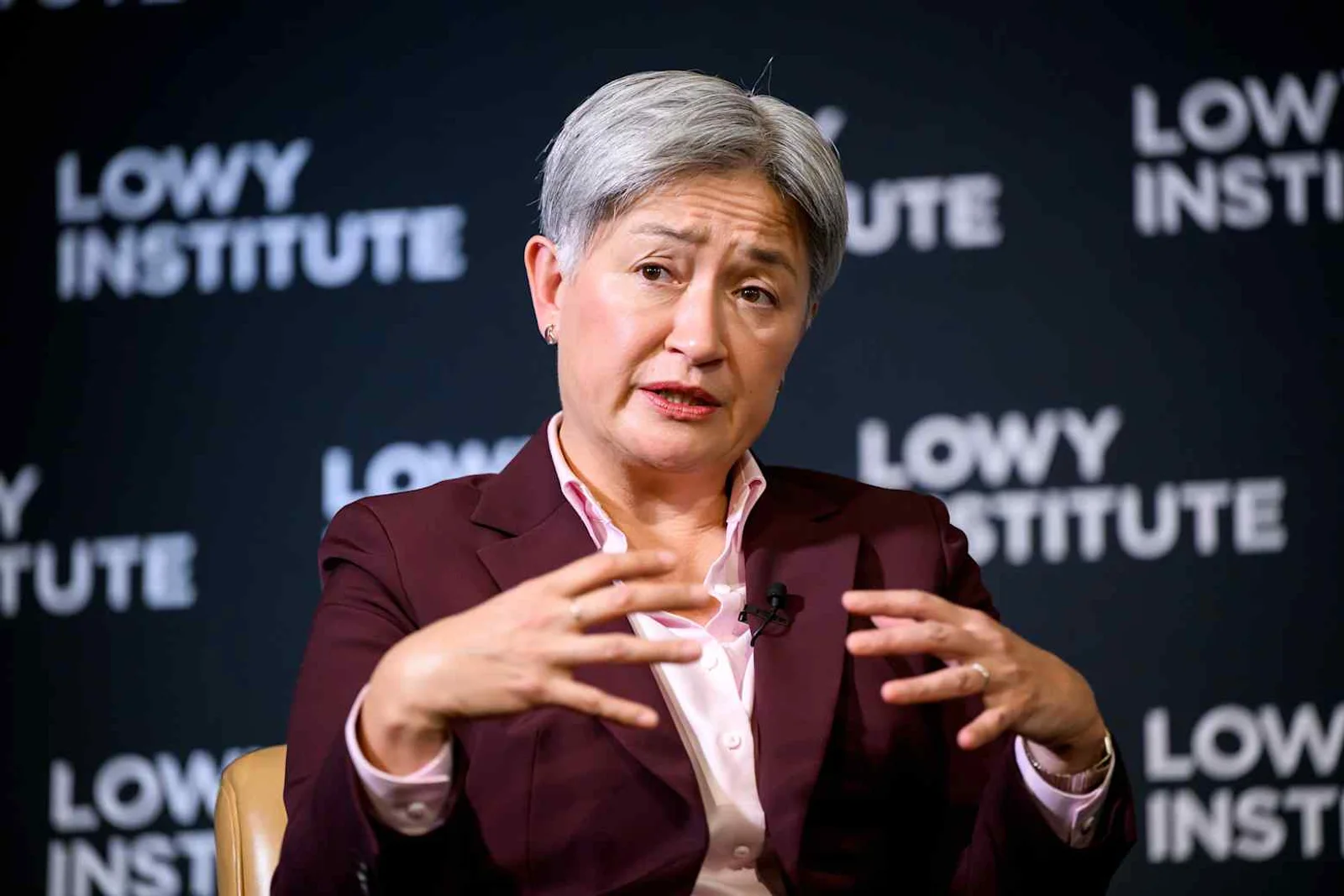 Australian Foreign Minister Penny Wong gestures with both hands while speaking in front of a Lowy Institute backdrop